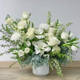 White floral arrangement in a white vase with roses and mixed blooms