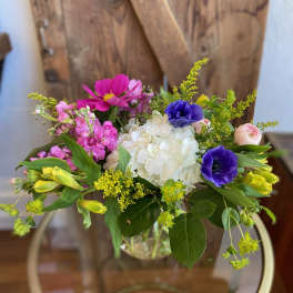 Colorful mixed bouquet with white hydrangea, purple anemones, and pink blooms in a clear glass vase