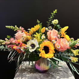 Mixed bouquet of roses, sunflowers, tulips, and snapdragons in a rainbow glass vase