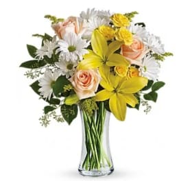 Bouquet of yellow lilies, white daisies, and peach roses in a clear glass vase