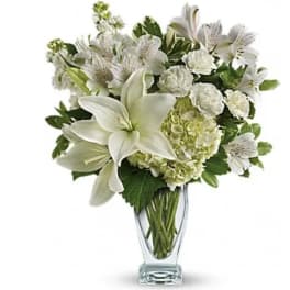 White lilies and mixed white flowers in a clear glass vase