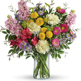 Tall mixed bouquet of yellow, pink, purple and white flowers in a clear glass cylinder vase