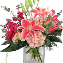 Pink lilies, hydrangeas, and tulips arranged in a clear rectangular glass vase