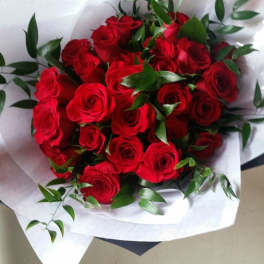Bouquet of red roses wrapped in white paper with green foliage