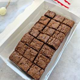 Box of chocolate brownies cut into squares with a cake slice nearby