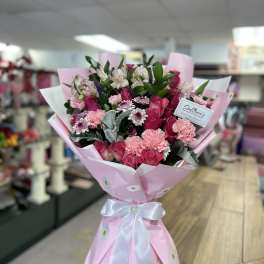 Pink bouquet of roses, carnations, and small daisy-like flowers wrapped in pink paper