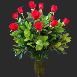 Red roses arranged in a clear glass vase with dense greenery