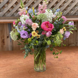 Mixed bouquet of pink, purple, white, and yellow flowers in a clear glass vase