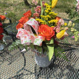 Bouquet of orange roses, yellow tulips, and pink snapdragons in a silver vase