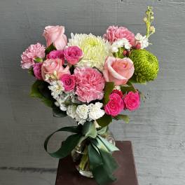 Pink and white mixed bouquet in a glass vase with a green ribbon