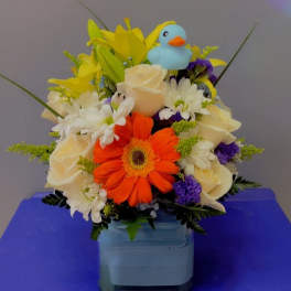 Mixed bouquet with orange gerbera, white roses, and a blue duck topper in a vase