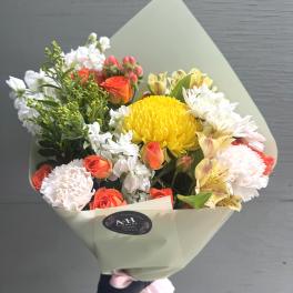 Bouquet of yellow, orange, and white flowers wrapped in pale paper