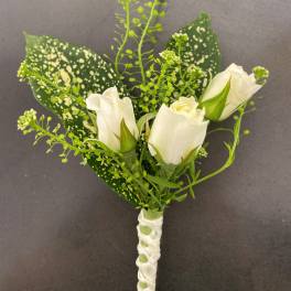 White rose boutonniere with speckled green leaves and ribbon wrap