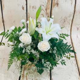 White lilies and roses arranged with greenery in a basket