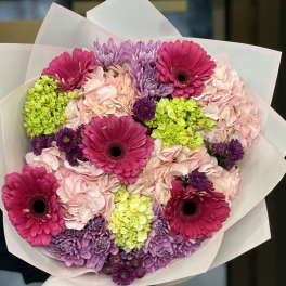 Bouquet of pink gerbera daisies, hydrangeas, and purple chrysanthemums wrapped in white paper