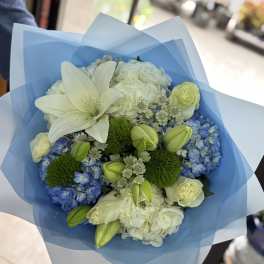 Bouquet of white lilies, blue hydrangeas, and pale roses wrapped in blue paper