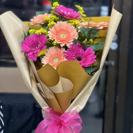 Bouquet of pink and peach gerbera daisies wrapped in cream paper with a pink ribbon