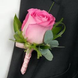 Pink rose boutonniere with green foliage on a black suit