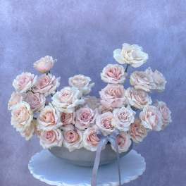 Arrangement of pale pink and white roses in a shallow bowl with a ribbon