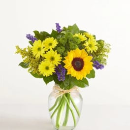 Yellow daisies and a sunflower in a clear glass vase