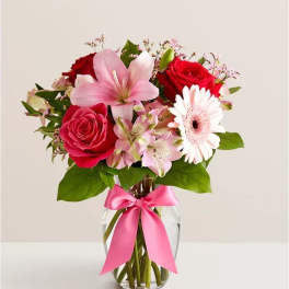 Bouquet of red roses, pink lilies, and a white gerbera daisy in a glass vase