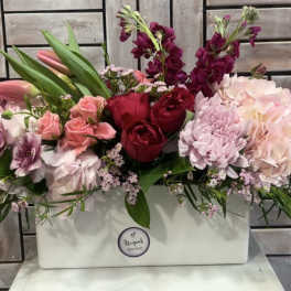 Mixed pink and red flowers arranged in a white rectangular box