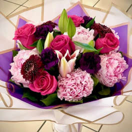 Bouquet of pink roses, lilies, and purple flowers wrapped in white and purple paper