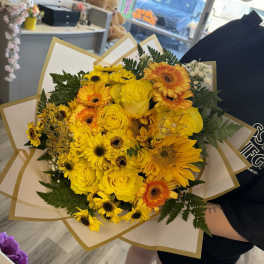 Yellow bouquet of roses and gerbera daisies wrapped in white paper