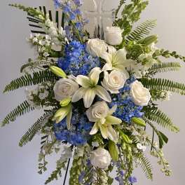Tall floral spray with white roses, lilies, and blue flowers around a clear cross