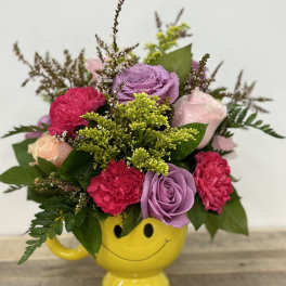 Mixed pink and purple bouquet in a yellow smiley-face mug