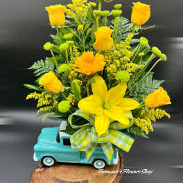 Yellow roses and a lily arranged in a turquoise truck planter