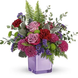 Purple and pink flower arrangement in a lavender glass vase