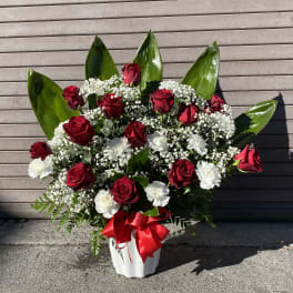 Red roses and white carnations in a white vase with a red ribbon