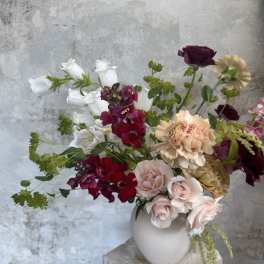 Mixed bouquet of roses, carnations, and white bell-shaped flowers in a white vase
