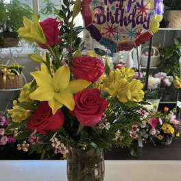 Birthday bouquet of red roses and yellow lilies in a glass vase with a balloon