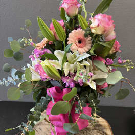 Pink roses, lilies, and a gerbera daisy in a glass vase with a pink ribbon