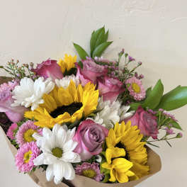 Bouquet of pink roses, sunflowers, and white daisies wrapped in brown paper