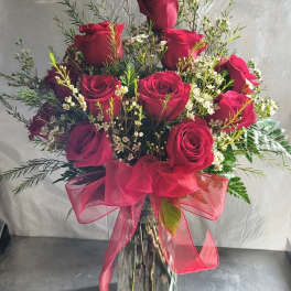 Red roses in a clear glass vase with a pink ribbon