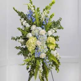 Tall floral standing spray with white, blue, and green blooms on an easel