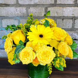 Yellow roses and a gerbera daisy in a green glass vase