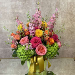 Colorful bouquet of pink, orange, and yellow flowers in a green box with a gold ribbon