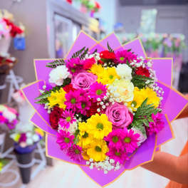 Bouquet of pink, yellow, white, and red flowers wrapped in purple paper