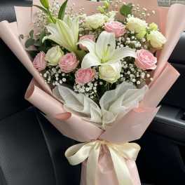 Bouquet of pink and white roses with white lilies wrapped in pink paper
