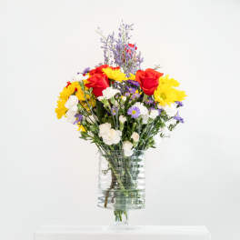 Mixed bouquet of red roses, yellow daisies, and white flowers in a clear glass vase