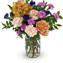 Mixed bouquet of roses, carnations, and purple filler flowers in a glass vase