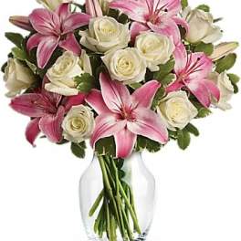 Pink lilies and white roses arranged in a clear glass vase