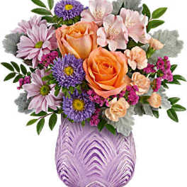 Bouquet of orange roses, pink flowers, and purple daisies in a lavender vase