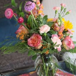 Mixed bouquet of pink, peach, purple, and yellow flowers in a clear glass vase