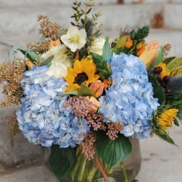 Mixed bouquet with blue hydrangeas, sunflowers, and tulips in a glass vase