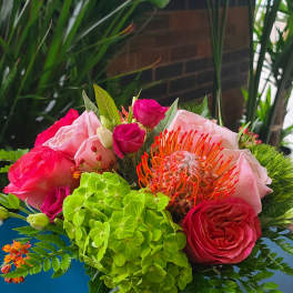 Bouquet of pink roses, green hydrangea, and orange pincushion protea in a vase
